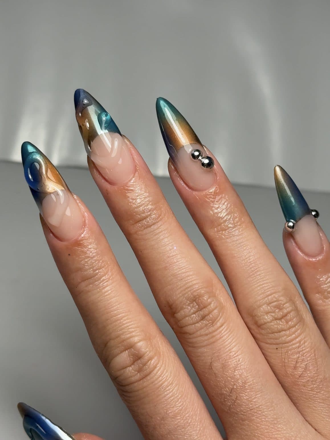 Stiletto Gel-X nails with blue and bronze aura chrome tips and silver beads