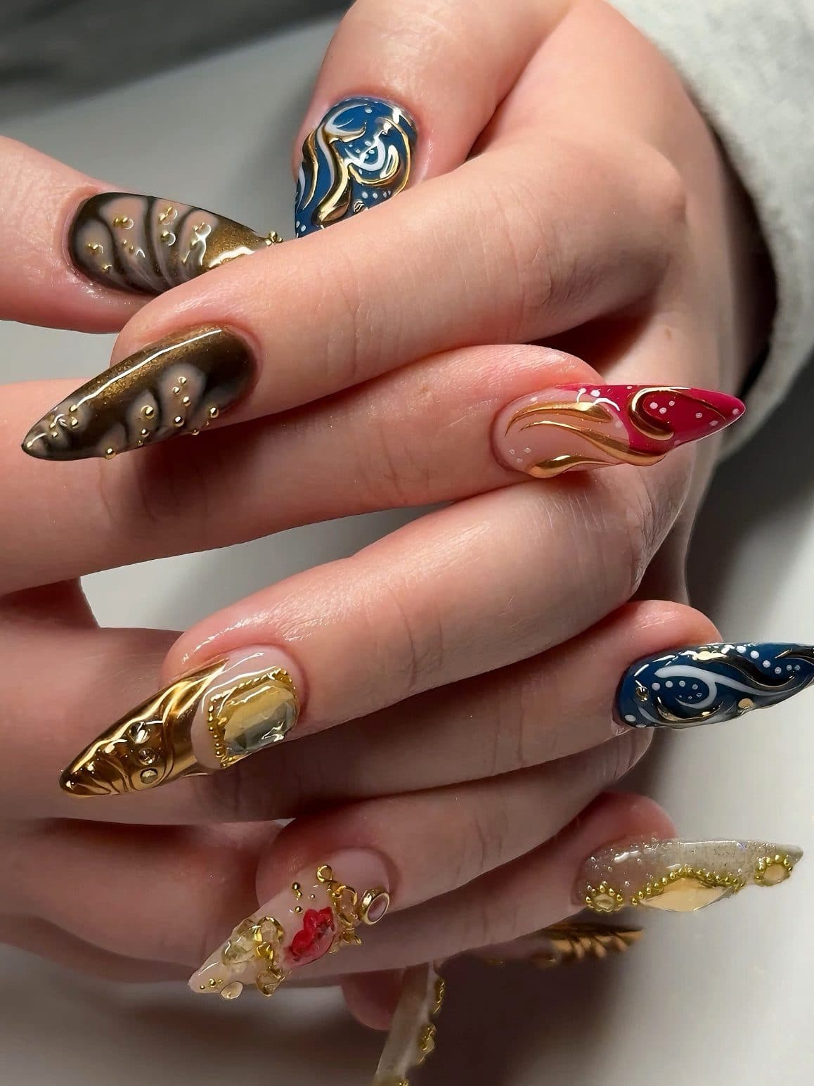 Stiletto Gel-X set with gold chrome, blue swirl art, red accents and 3D gold detailing